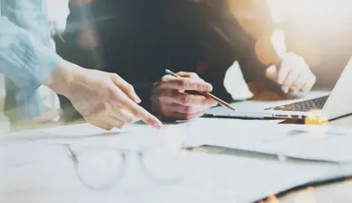 People looking at computer and documents. One pointing one with pen in their hand.