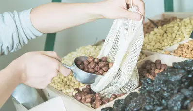 someone refilling reusable bag with produce (nuts & dates)