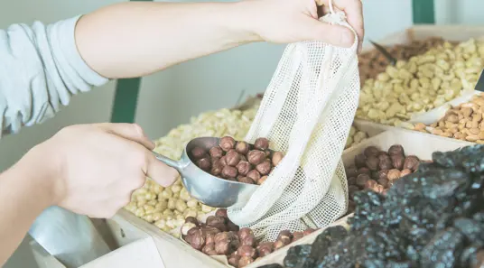 someone refilling reusable bag with produce (nuts & dates)