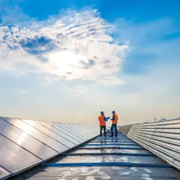 Two men on roof with solar panels, both wearing PPE