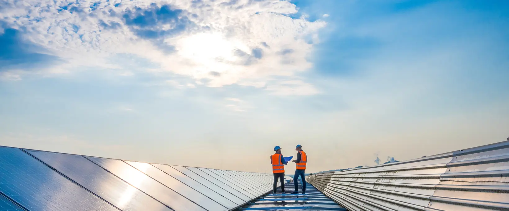 Two men on roof with solar panels, both wearing PPE