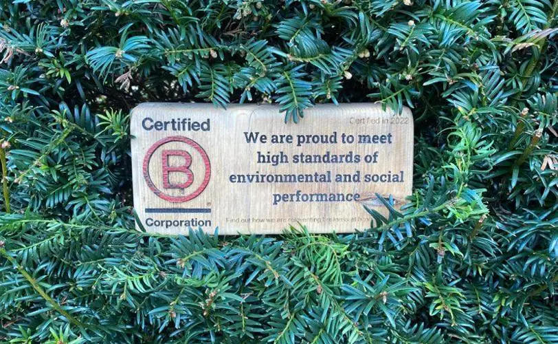 B Corp certification sign displayed on green foliage.