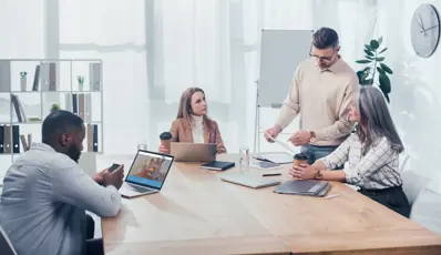 Team meeting, four people in a meeting room with laptops and documents