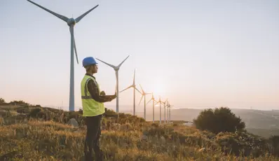 Man stood near windmills, on a hilltop wearing PPE and holding a clipboard