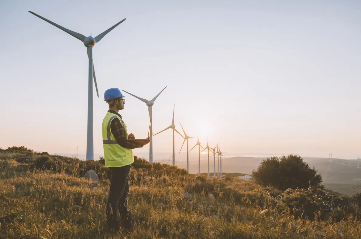 Man stood near windmills, on a hilltop wearing PPE and holding a clipboard